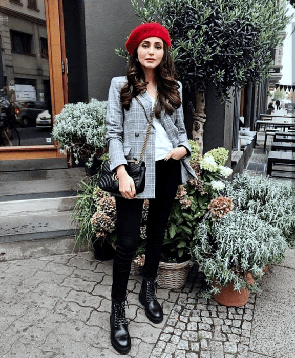 chica de cabello castaño usando un beret rojo, blazer gris de cuadros, top blanco, skinny jeans negros y botines negros de piso, bolso negro de cuero