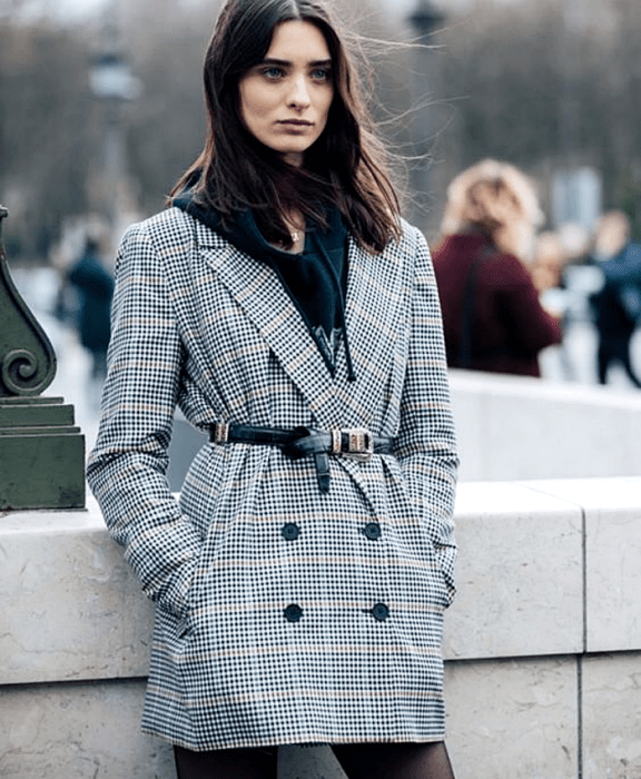 chica de cabello oscuro usando una sudadera negra, blazer gris de cuadros, cinturón negro de piel, medias semi-transparentes