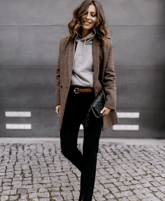 chica de cabello castaño usando una sudadera gris, blazer café de cuadros, cinturón café, pantalones de vestir negros, bolso de mano negro 