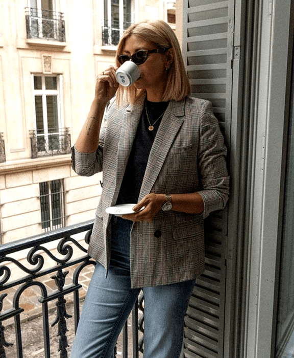 chica rubia usando lentes de sol, top negro, blazer café de cuadros, jeans a la cintura tomando café