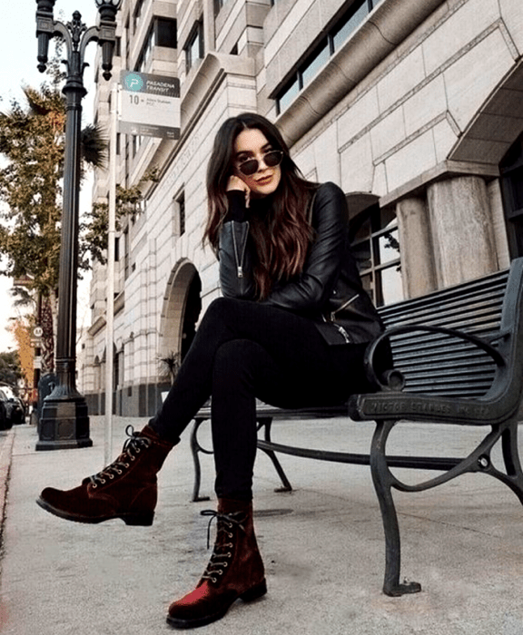 chica de cabello castaño usando lentes de sol, suéter negro de manga larga, chaqueta de cuero negro, botines rojos de terciopelo rojo