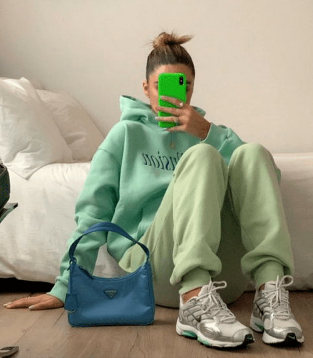 chica de cabello claro usando una sudadera oversized verde pistache, pants verde pastel, tenis grises con blanco y bolso azul de mano