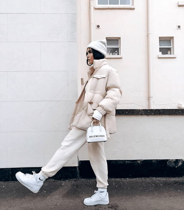 chica de cabello negro usando un gorro beanie blanco, chamarra puffer jacket beige, pants deportivos beige, tenis blancos, top de manga larga blanco y bolso de mano blanco mini