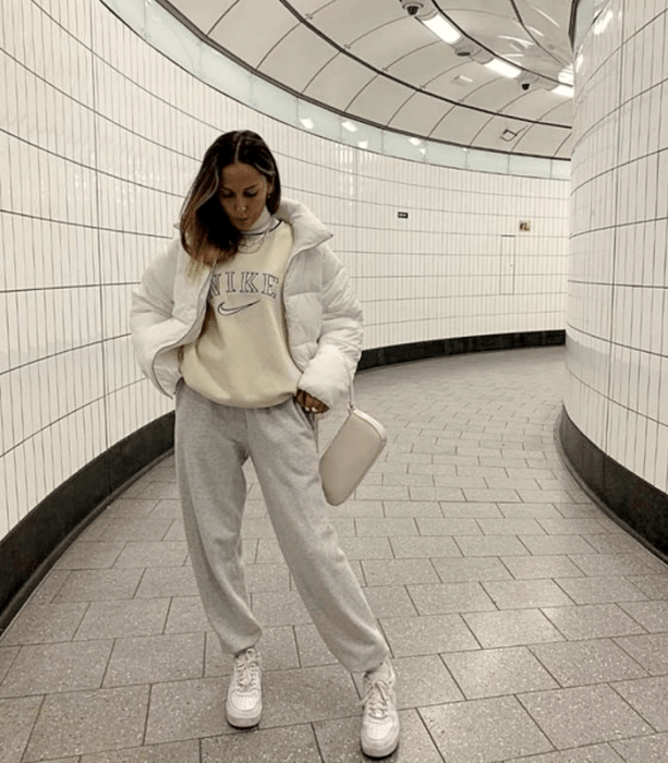 chica de cabello claro usando una sudadera blanca nike, chamarra blanca, pants grises, tenis blancos y bolsa de mano blanca