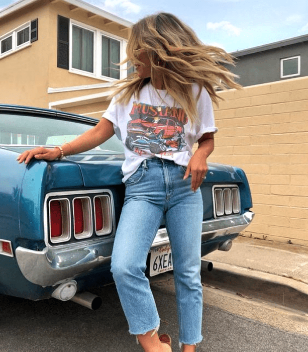 chica rubia usando una camiseta blanca gráfica estampada, jeans a la cintura y sandalias metálicas