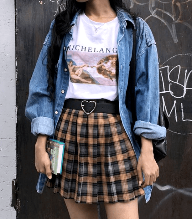 chica de cabello castaño usando una camiseta blanca gráfica estampada, camisa de mezclilla de botones, cinturón negro con hebilla de corazón, minifalda de cuadros naranja con azul