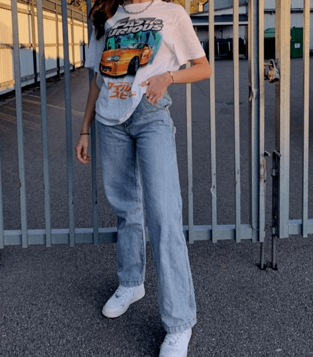 chica de cabello castaño usando una camiseta blanca gráfica estampada, jeans holgados y tenis deportivos