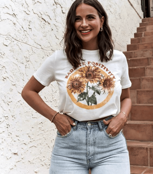 chica de cabello castaño corto usando una camiseta blanca estampada, jeans a la cintura ajustados