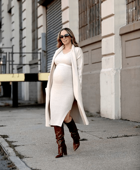 chica rubia embarazada, con lentes de sol, vestido largo tejido beige, abrigo largo beige, botas largas de tacón de piel rojas