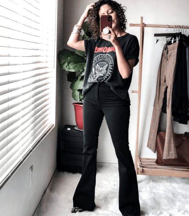 chica de cabello chino usando una camiseta de ramones negra, jeans negros acampanados, botines de piel de animal print