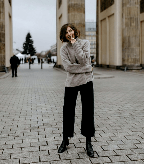 chica de cabello castaño usando un suéter beige, jeans negros acampanados, botines de tacón