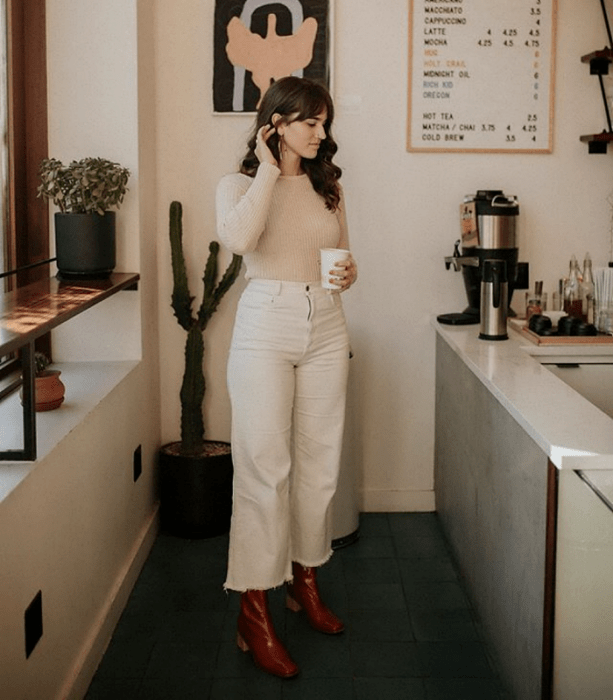 chica de cabello castaño usando un suéter beige, pantalones tipo culotte blancos, botines de cuero café