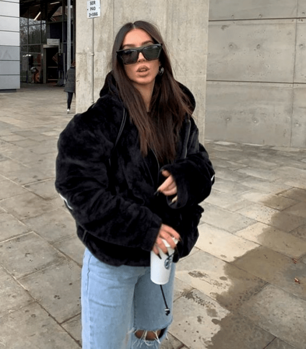 chica de cabello largo usando lentes de sol, abrigo oversized negro afelpado, jeans holgados