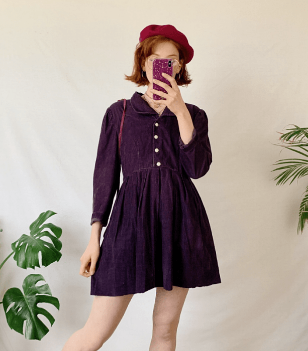 chica pelirroja usando un vestido de pana morado con botones al frente y cuello, beret rosa