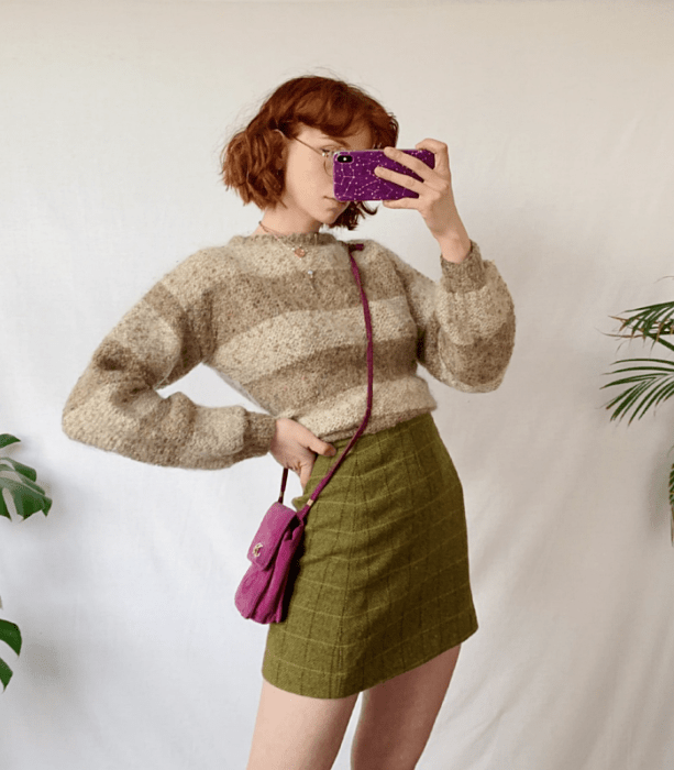 chica pelirroja usando un suéter beige de rayas, minifalda verde a cuadros, bolso crossbody bag fucsia