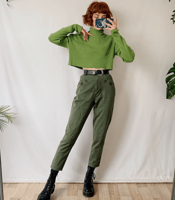 chica pelirroja usando un suéter verde de cuello alto y manga larga, cinturón negro, pantalón a la cintura color verde, botas negras de plataforma gruesa