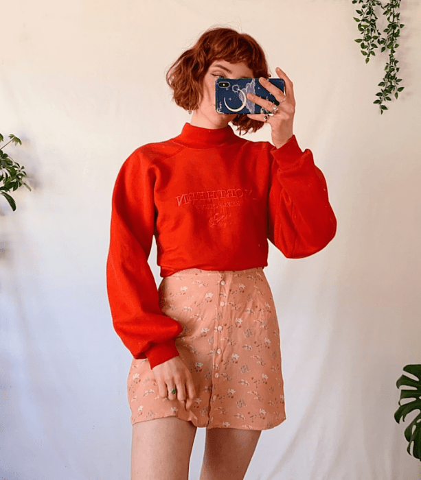 chica pelirroja usando una sudadera roja de cuello alto y manga larga, minifalda rosa con flores blancas