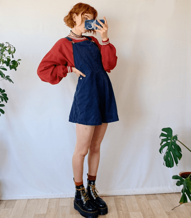 chica pelirroja usando una sudadera roja, vestido de overol azul de mezclilla y botas negras de plataforma