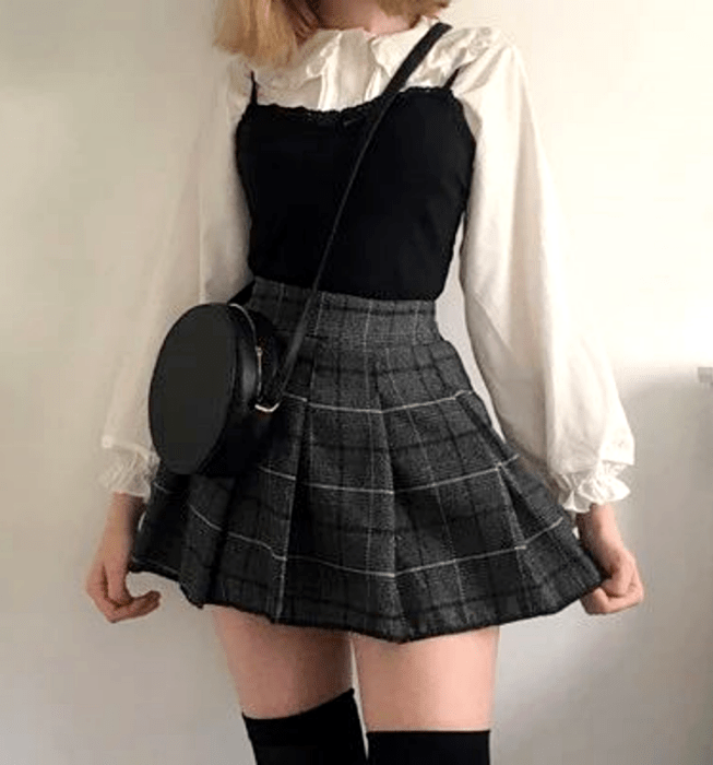 chica rubia usando una camisa blanca de mangas abombadas, top negro de tirantes, minifalda gris de cuadros estilo escocesa con tablones, medias  negras largas y bolso negro crossbody bag