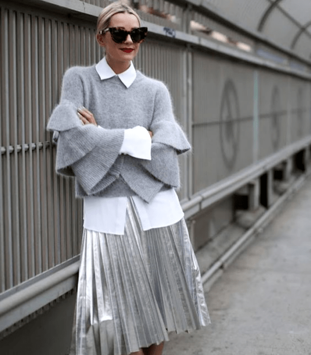 chica rubia usando lentes de sol, suéter gris con mangas holgadas, camisa de vestir blanca, falda larga de tablones metálica plateada