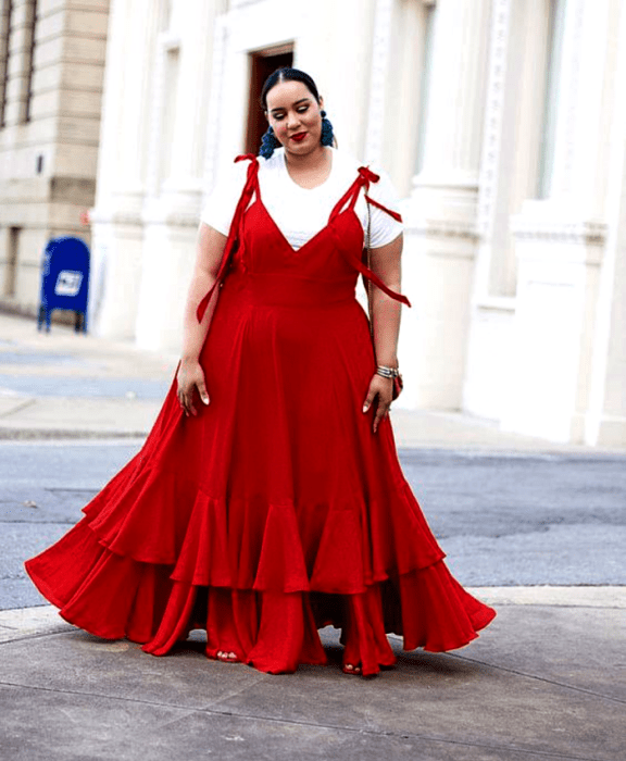 chica curvy morena con un vestido rojo de tirantes, escote en V, camiseta blanca debajo y falda con holanes