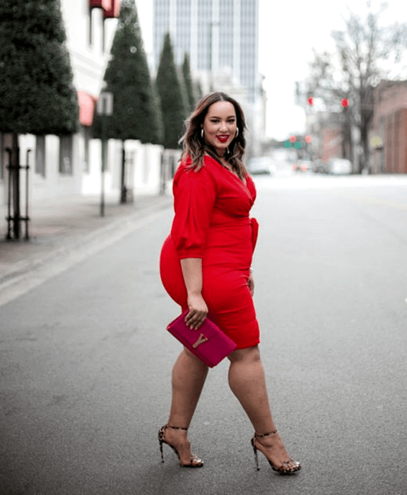 chica curvy de cabello castaño usando un vestido rojo de manga 3/4. cuello en v, bolso de mano fucsia y sandalias de animal print con tacón