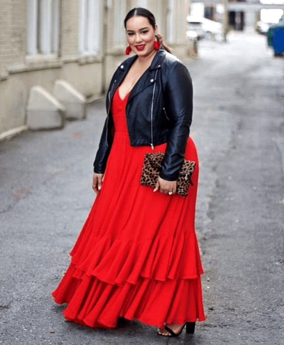 chica curvy usando un vestido rojo largo, cuello en V, con chaqueta de mezclilla negra, bolso de mano de animal print, sandalias negras de tacón