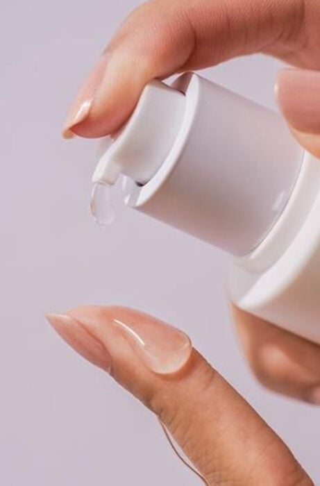 Mujer presionando un bote de serum para el rostro sobre su dedo