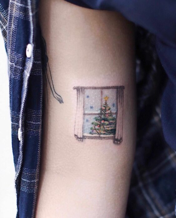 Chica con tatuaje en forma de ventana con un pino navideño; Tatuajes miniatura para las que aman la Navidad