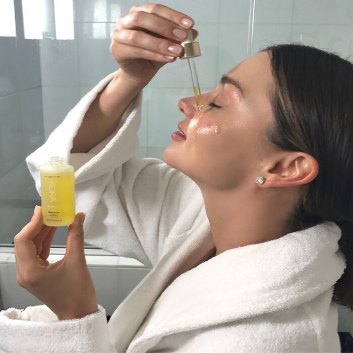 Miranda Kerr usando un aceite facial en su rostro con una bata de baño blanca