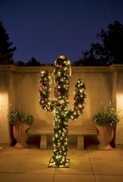 Árbol de navidad en forma de cactus colocado en el exterior de la casa decorado con luces amarillas y esferas rojas