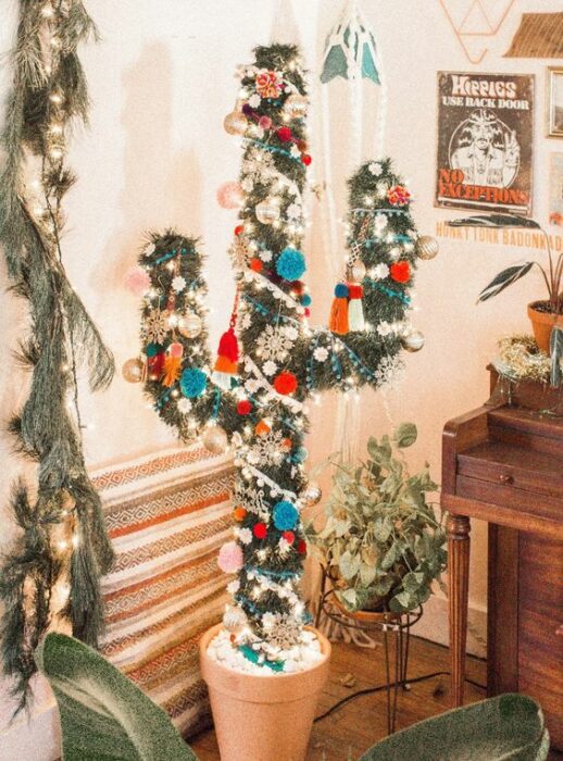 Árbol de navidad en forma de cactus  en una sala de paredes blancas con un mueble de madera en un costado