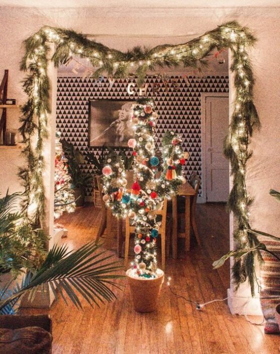 Árbol de navidad en forma de cactus en medio del comedor y la sala con ramas de pino y luces decorando la parte superior del techo