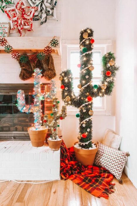 Árboles de navidad en forma de cactus de color verde y blanco en una sala con paredes blancas cerca de una chimenea