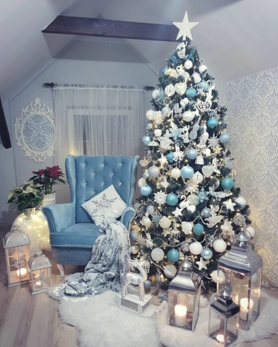 Árbol de navidad verde con esferas turquesas y blancas al lado de un sillón azul en una habitación con muros blancos