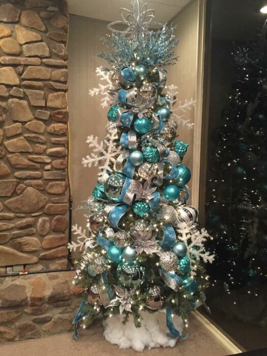 Árbol de navidad blanco con copos grandes blancos y esferas grandes azul Tiffany en una habitación con pared de piedraa en una habitación con pared de piedra