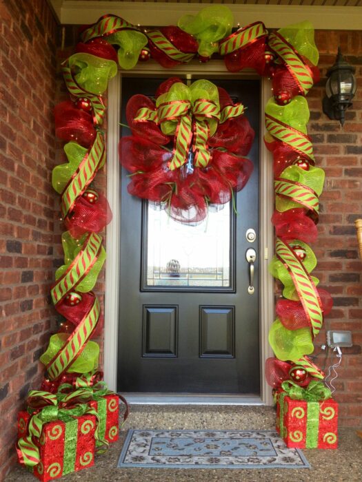 Decoración navideña en una puerta hecha con moños de color rojo con verde 