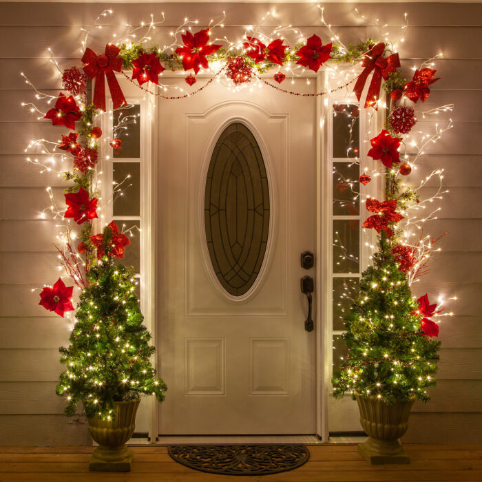 Decoración navideña hecha con luces, pinos y moños de color rojo 