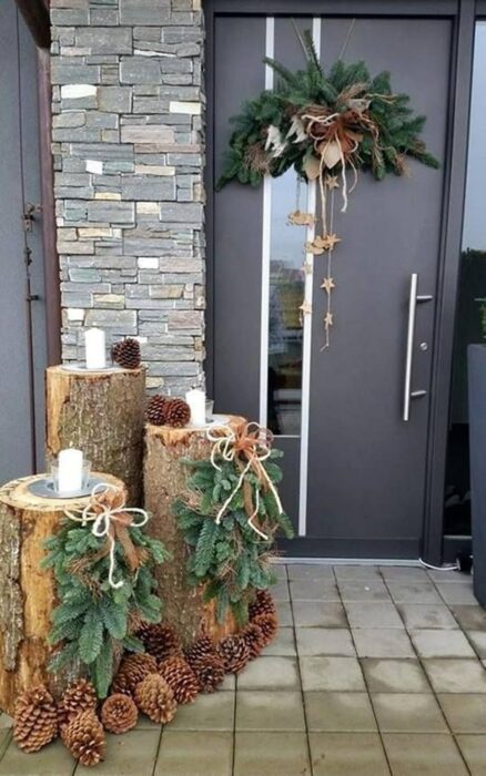 Puerta de una casa decorada con troncos y velas y una corona en la puerta