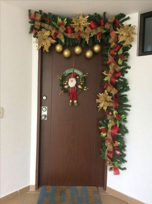 Decoración navideña en una puerta hecha con guirnaldas en colro café con verde y esferas rojas