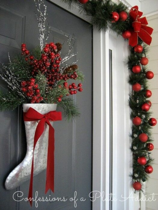 Decoración navideña en una puerta hecha con guia de color verde, esferas rojas y una bota plateada 