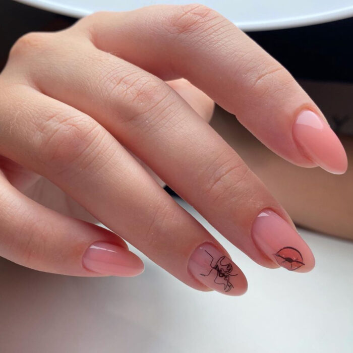 Manos de mujer con uñas largas en forma de almendra, pintadas con esmalte color nude rosa, con diseño de labios y de personas dándose un beso