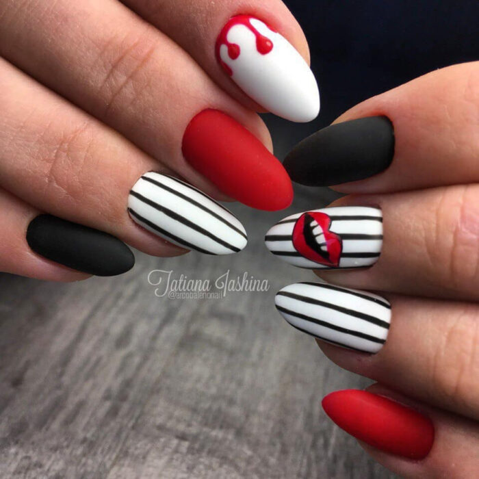 Manos de mujer con uñas largas en forma de almendras pintadas con esmalte mate de colores blanco, rojo y negro con diseños de rayas verticales y labios sonriendo