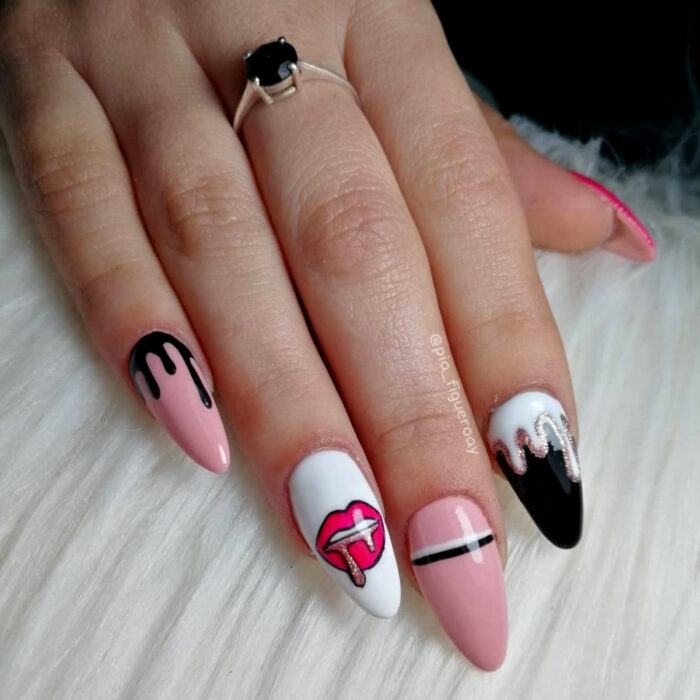 Manos de mujer con uñas largas stiletto pintadas con esmalte de colores rosa bebé, negro y blanco con diseño de labios con glitter