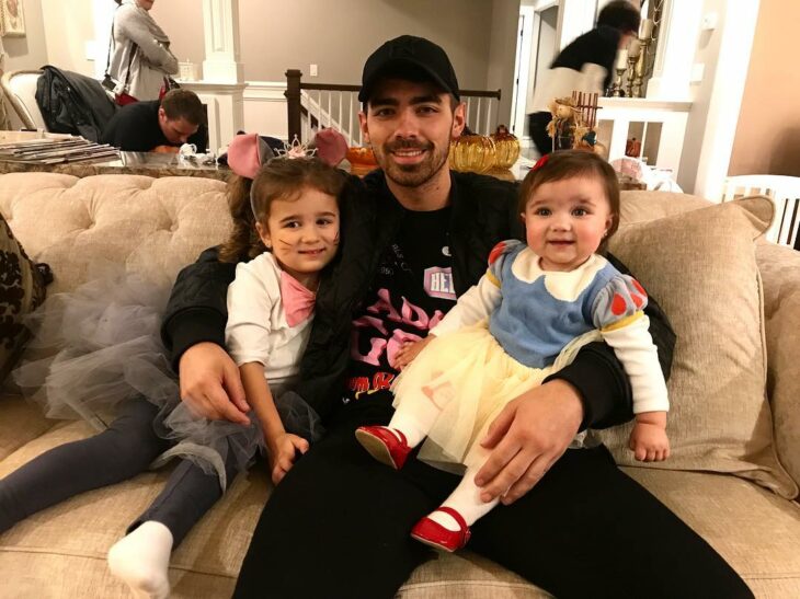 Joe Jonas sentado junto a sus sobrinas mientras están jugando 