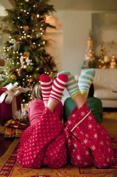 Dos pares de pies usando pijamas y calcetines de navidad con el árbol de navidad de fondo