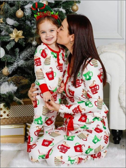 Mujer y niña usando la misma pijama, la mujer le besa la mejilla a la nula y con el árbol de navidad detrás de ambas