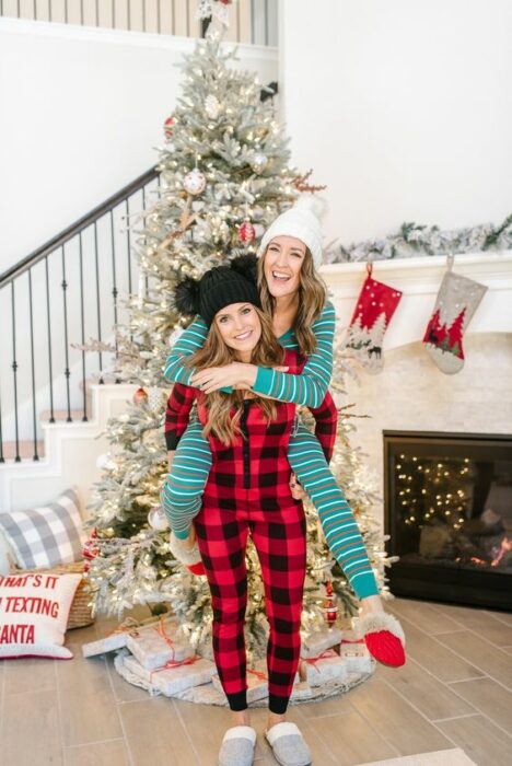 Amigas usando pijamas de navidad, posando delante del árbol mientras se divierten