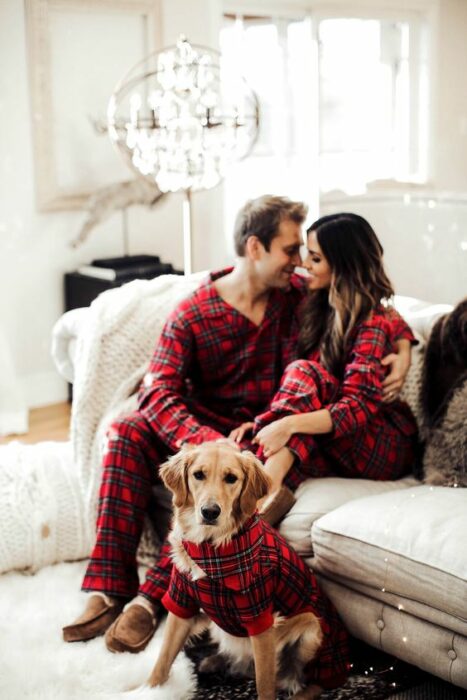 Hombre, mujer y perro con pijamas rojas de cuadros sentados en un sillón grande blanco