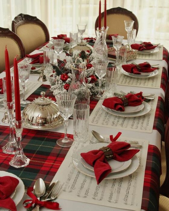 Mesa decorada con cubiertos blancos, moños rojos y manteles a juego; Ideas para decorar la mesa en Navidad